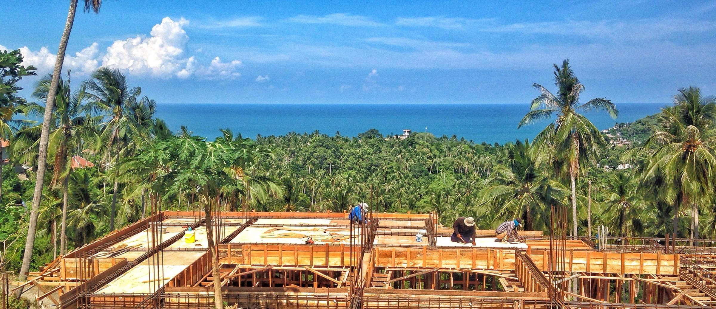 The HAMPKON construction crew on site, structural frame rising above the treeline with a view to the Gulf of Thailand, Koh Samui